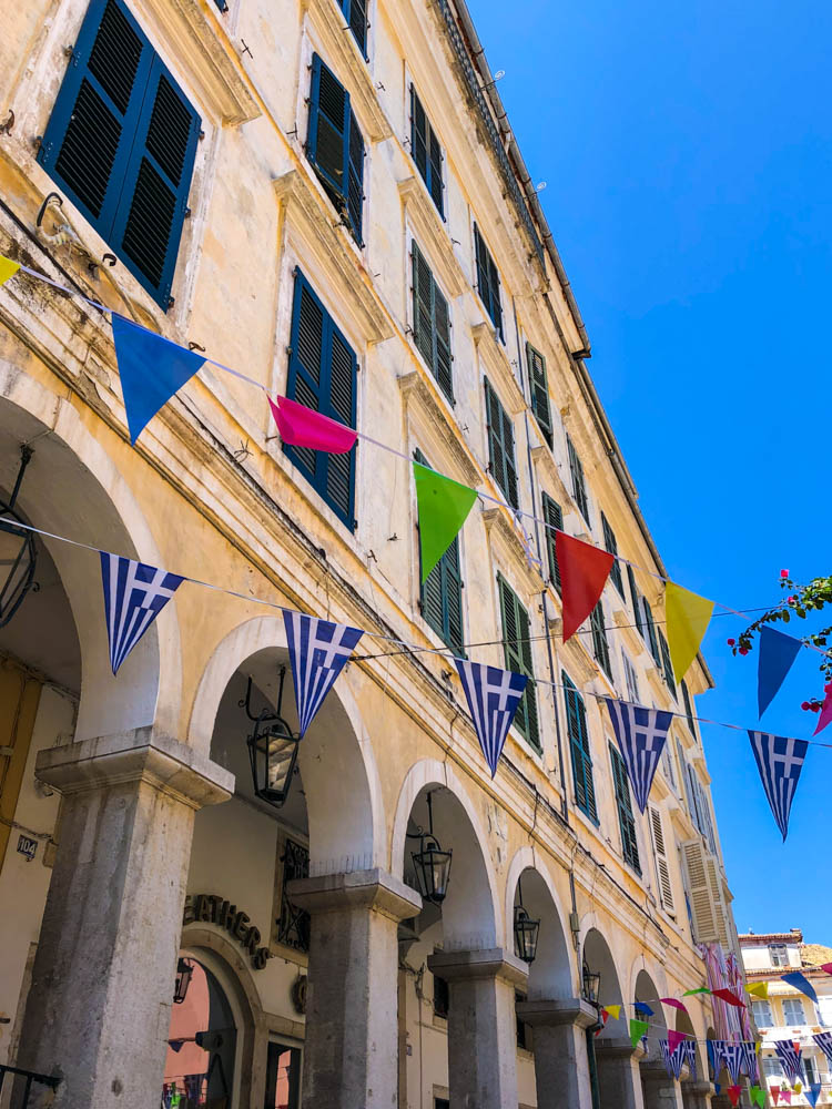 Es hängen bunte Fähnchen über eine Gasse in Korfu. Altstadt Häuserfassade. Der Himmel ist kräftig blau