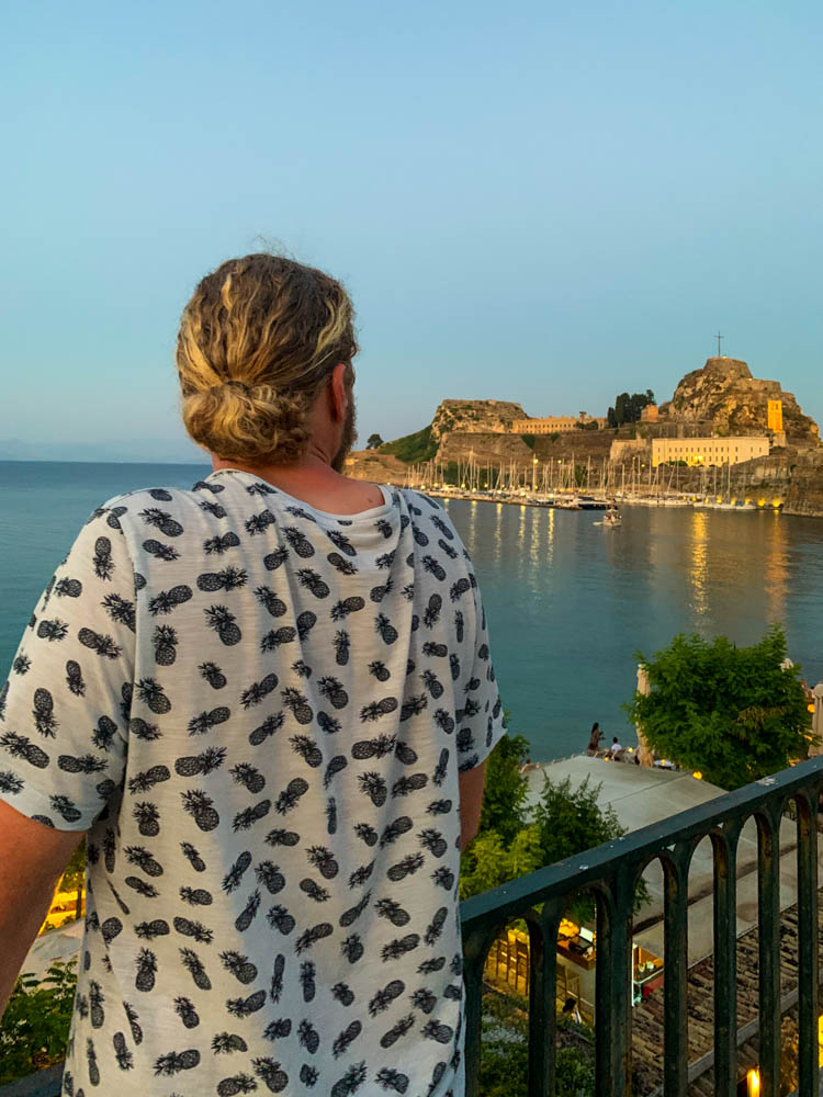 Julian blickt auf die alte Festung in Korfu. Der Sonnenuntergang beleuchtet die Stadt in gelbe Töne