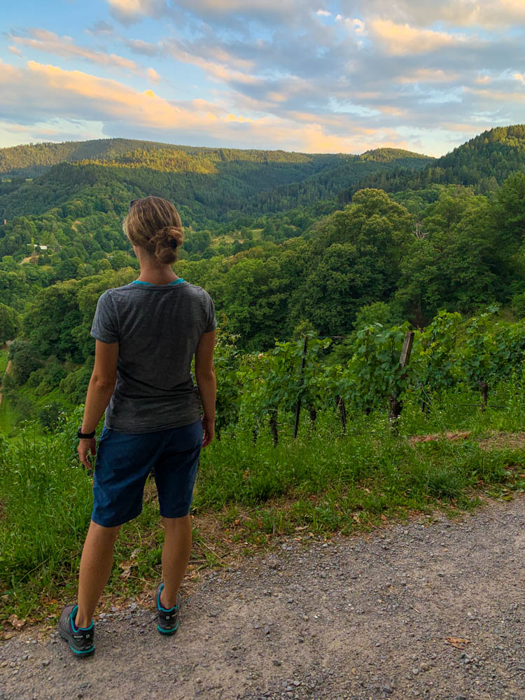 Melanie blickt ins Tal bei Obertsrot im Schwarzwald und genießt die kleine Auszeit. Weinreben vor ihr und viel grün rund herum