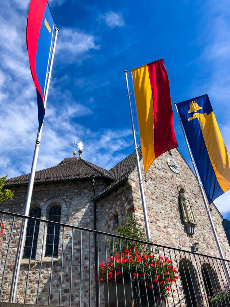 Eine Liechtensteiner Kirche mit verschiedenen bunten Flaggen davor.