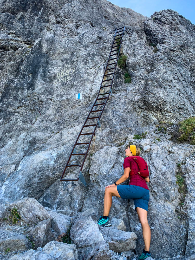 Wanderungen in Liechtenstein. Melanie auf Drei Schwestern Steig. Sie muss als nächstes über eine Leiter aufsteigen, zu welcher sie aufblickt. Felsiges Gelände mit Leiter