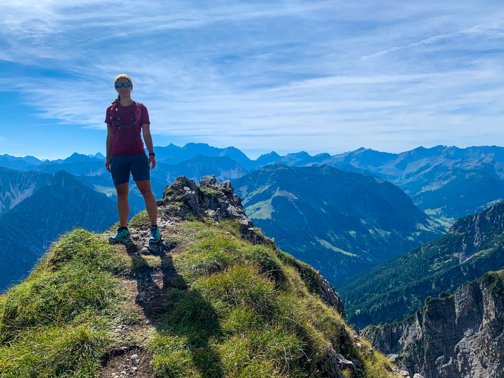 Wanderungen in Liechtenstein. Melanie im Abstieg vom Garsellakopf - Drei Schwestern Steig. Berglandschaft im Hintergrund. Sie grinst in die Kamera