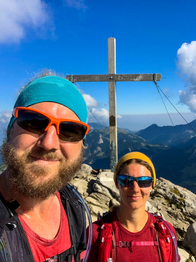Wanderungen in Liechtenstein mit Ausblick. Selfie von Melanie und Julian am Augstenberg. Das Gipfelkreuz ist hinter bzw. zwischen ihnen zu sehen.