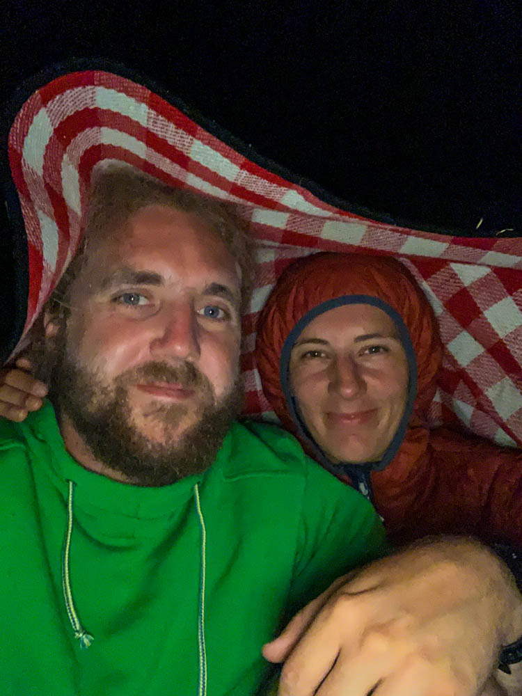 Selfie von Melanie und Julian. Sie schützen sich mit einer Picknickdecke vom Regen.