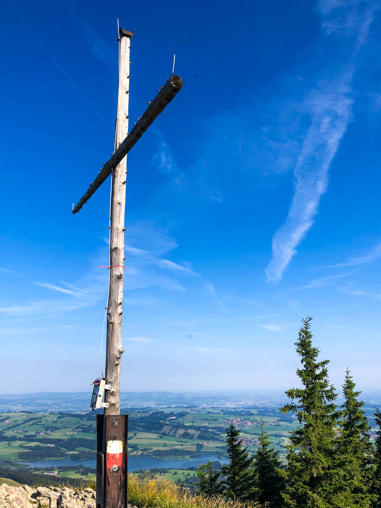 Touren im Allgäu - Gipfelkreuz Alpspitze bei Nesselwang. Im Tal sind einige Felder zu sehen, der Himmel ist kräftig blau.