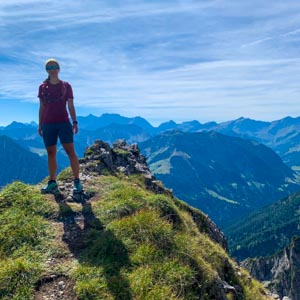 Wanderungen in Liechtenstein. Melanie im Abstieg vom Garsellakopf - Drei Schwestern Steig. Berglandschaft im Hintergrund. Sie grinst in die Kamera