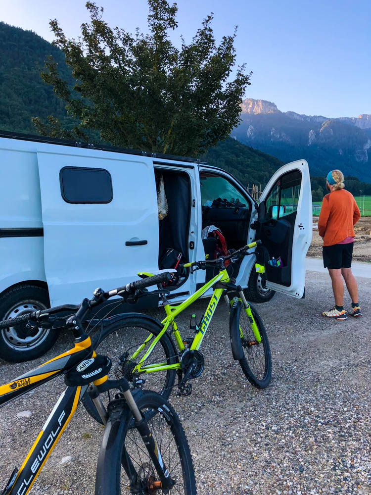 Mit den Rädern zur Wanderung in Aschau im Chiemgau. Julian steht neben Van Vivaldi und blickt auf die Berge. Die Fahrräder stehen direkt daneben.