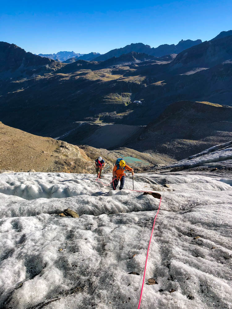 Julian auf dem Ochsentaler Gletscher im Aufstieg zum Piz Buin in der Seilschaft. Der Himmel ist kräftig blau. Blick außerdem ins Tal und auf das Bergpanorama