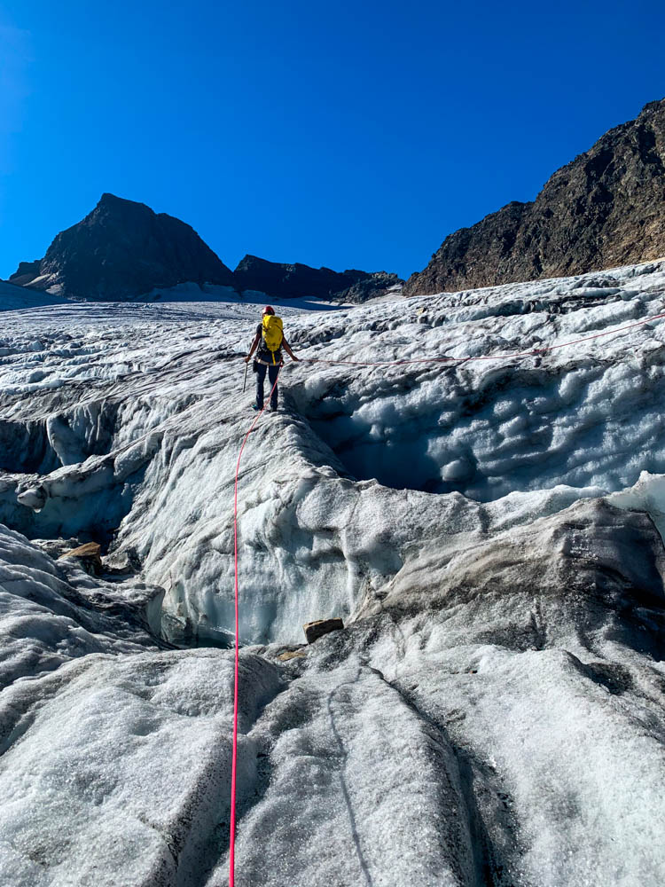 Melanie auf dem Ochsentaler Gletscher im Aufstieg zum Piz Buin in der Seilschaft. Der Himmel ist kräftig blau. Rechts und links von ihr sind tiefe Spalten zu sehen.