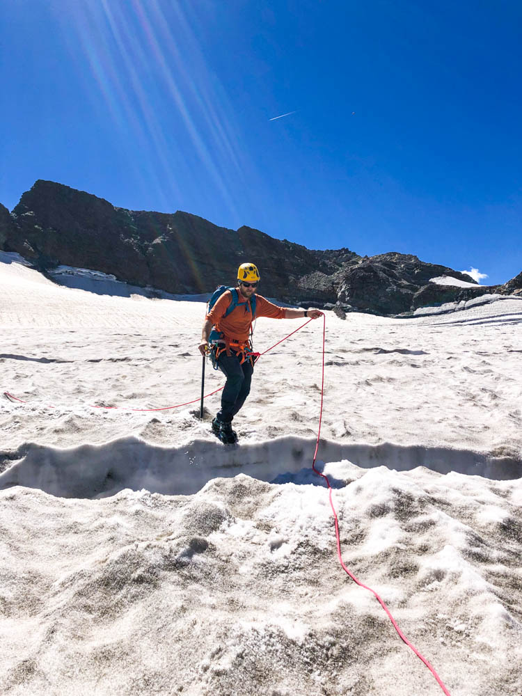 Julian springt über eine Spalte im Ochsentaler Gletscher nach der Piz Buin Besteigung. Der Himmel ist kräftig blau.