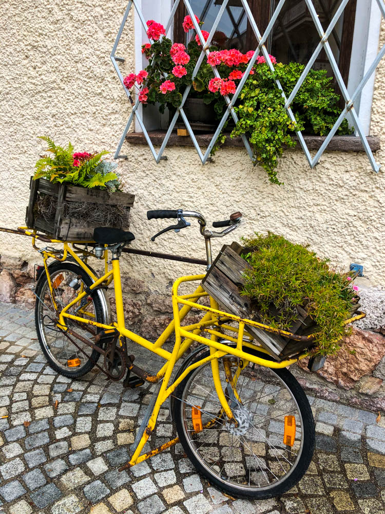 Gelbes Fahrrad mit Blumenschmuck auf Träger. Dekoration vor einem Haus in Ruhpolding in Bayern