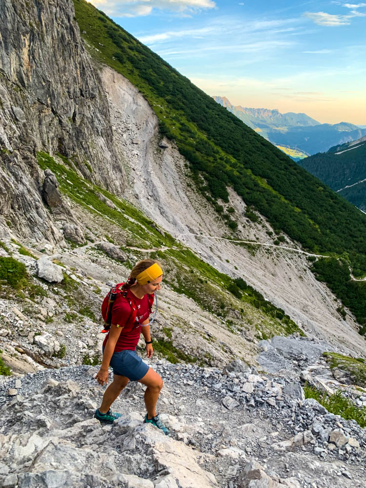 Wanderung Schesaplana Vorarlberg - Melanie im Aufstieg über Böser Tritt in Schottergelände. Im Tal sind die Berge orange verfärbt vom Sonnenaufgang.