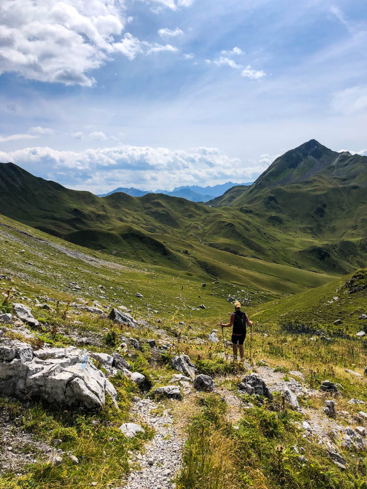 Julian wandert auf dem Prättigauer Höhenweg Richtung Gafalljoch in Vorarlberg. Das Tal ist schön grün und es sind ein paar Berge zu sehen.