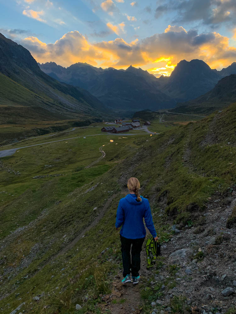 Sonnenuntergang Bielerhöhe Vorarlberg. Melanie läuft einen Pfad hinab und hält ein Klettergurt in der Hand.