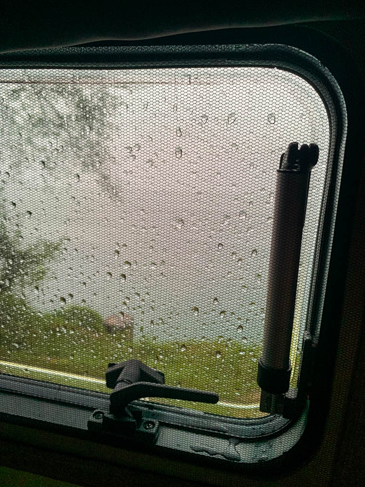 Regentag am Attersee. Blick auf den See durch Campingfenster, welches voller Regentropfen ist.