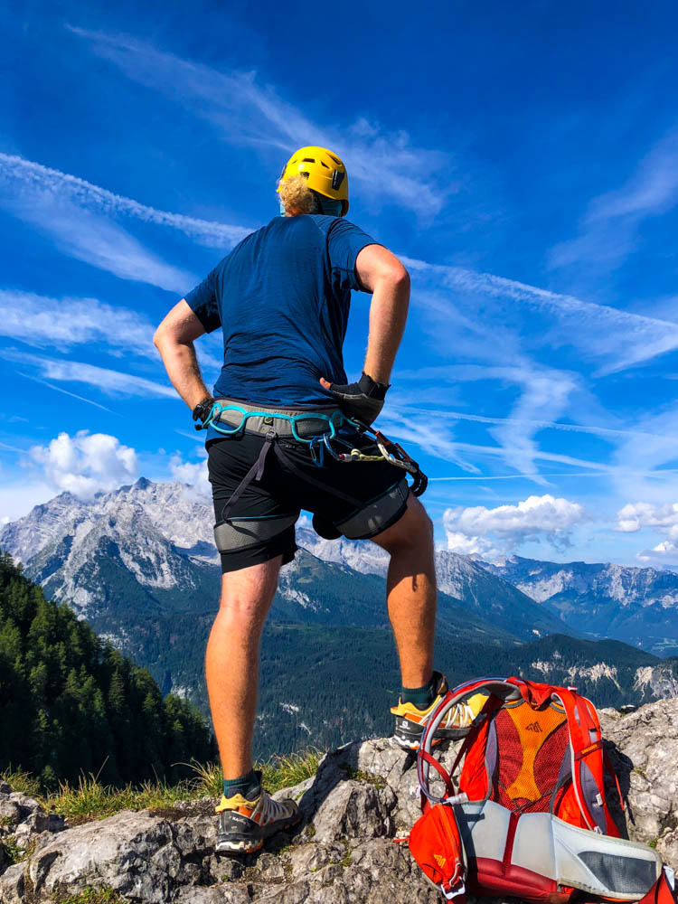 Julian am Gipfel des Kleinen Jenner nach dem Schützensteig Klettersteig. Er blickt auf die Berchtesgadener Alpen mit Blick u.a. auf den Watzmann. Der Himmel ist kräftig blau mit nur wenigen weißen Wolken