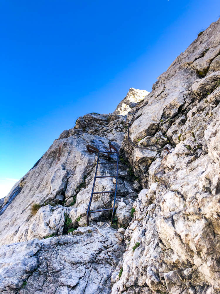 Eisenleiter und ein Drahtseil am Fels auf dem Weg zur Schärtenspitze. Der Himmel ist kräftig blau