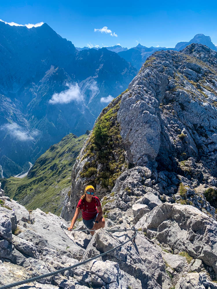 Melanie im Aufstieg zur Schärtenspitze im felsigen Gelände. Hinter ihr sind gut die Berchtesgadener Alpen zu sehen sowie der kräftig blaue Himmel.