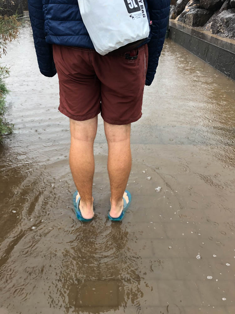 Julian steht mit seinen Flip-Flops im Wasser, welches auf der Straße steht. Regen auf Fuerteventura