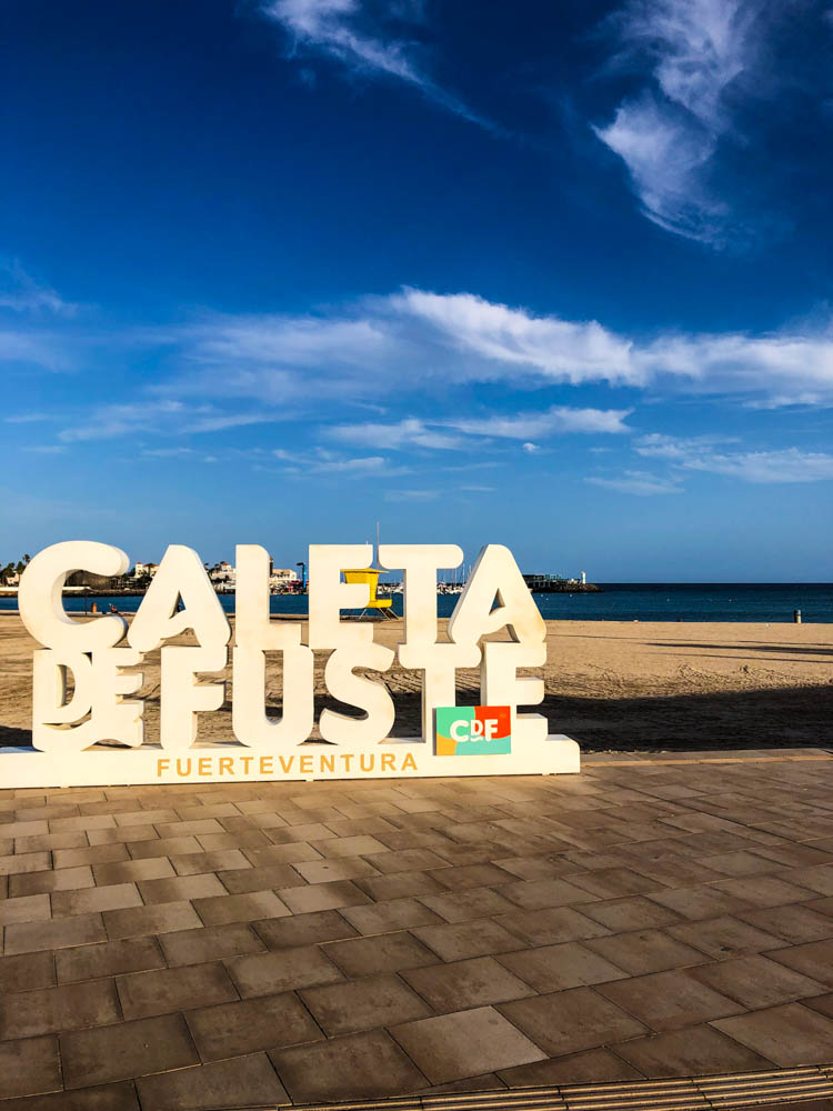 Caleta de Fuste Aufsteller am Strand der Stadt. Am Horizont ist das Meer sowie die Tauchbasis zu sehen. Der Himmel ist kräftig blau