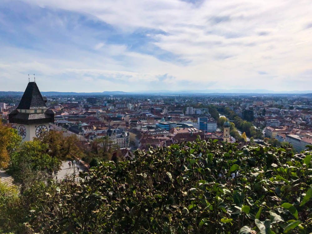 Blick vom Grazer Schlossberg auf die Stadt. Es sind ein paar wenige Wolken zu sehen, links sticht der Uhrturm ins Auge - querfeldein durch Österreich bis nach Graz