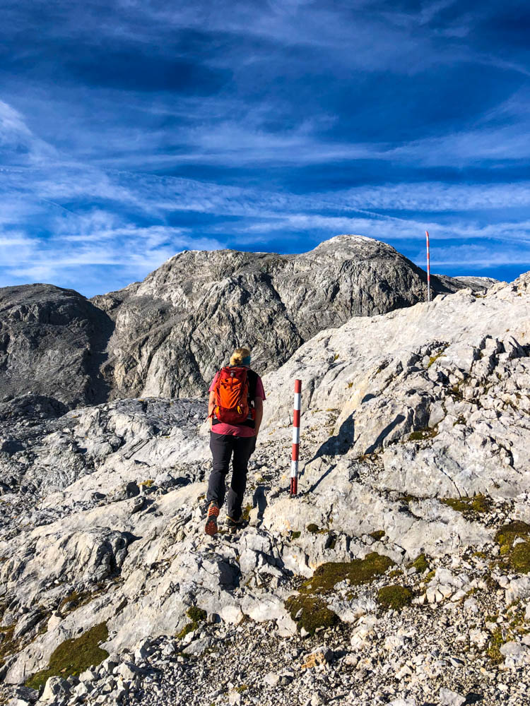 Julian in Felslandschaft auf dem Weg zum Hochkönig in den Berchtesgadener Alpen. Der Himmel ist kräftig blau mit ein paar Schleierwolken. Wegmarkierungen in Felsenlandschaft