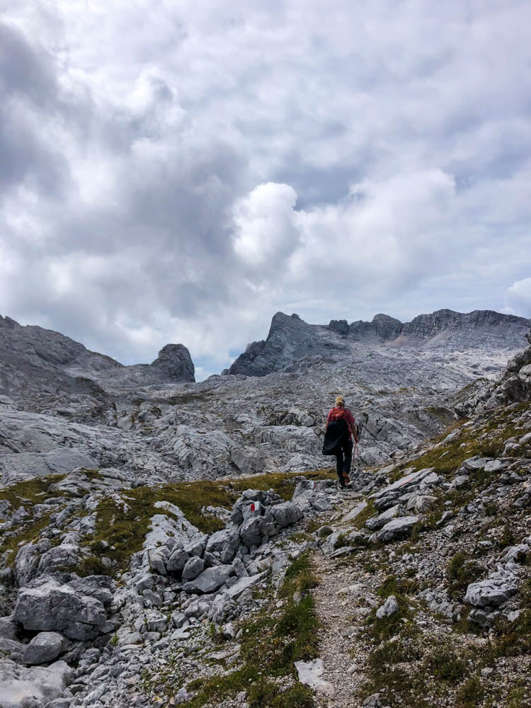 Julian läuft über Felsen im Steinernen Meer. Einem großen Felsenmeer in den Berchtesgadener Alpen. Er trägt in einer Hand seine Trekkingstöcke.