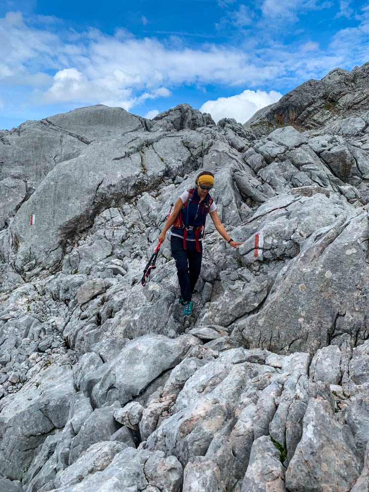 Melanie kletttert über Felsen im Steinernen Meer. Einem großen Felsenmeer in den Berchtesgadener Alpen. Sie hat in de einen Hand ihre Trekkingstöcke mit der anderen stützt sie sich am Fels ab.