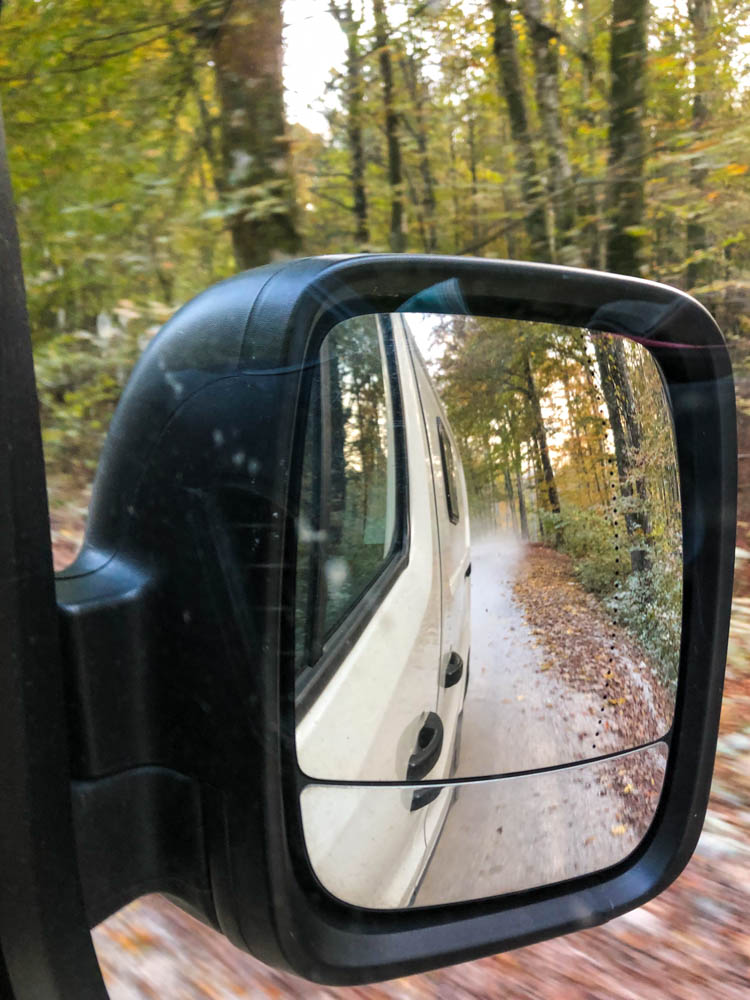 Van Vivaldi zu sehen durch den Seitenspiegel. Auto fährt durch einen slowenischen Wald, hinter dem Auto ist eine Staubwolke zu sehen.