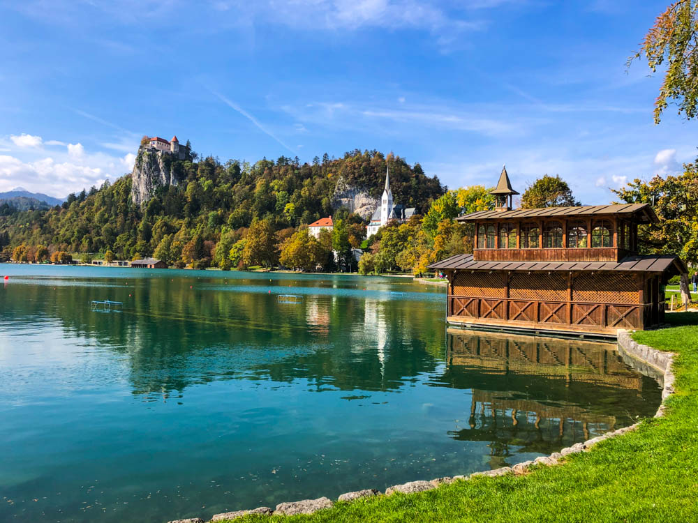 Im Bleder See spiegeln sich die Burg von Bled, die Kirche und weitere Gebäude im Wasser. Roadtrip Slowenien bei Sonnenschein