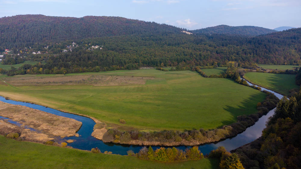 Naturschutzgebiet Cerkniško jezero in Slowenien. Aufnahme Karstsee von oben. Es sind viele grüne Wiesen zu sehen, sowie ein Fluss der sich durch die Wiese schlängelt. Am Horizont sind ein paar Hügel mit Bäumen zu sehen.