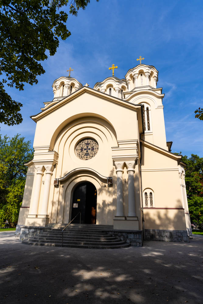 Kirche in Ljubljana mit drei Kirchtürmen, auf den jeweils ein Kreuz steht. Der Himmel ist kräftig blau. Roadtrip Slowenien