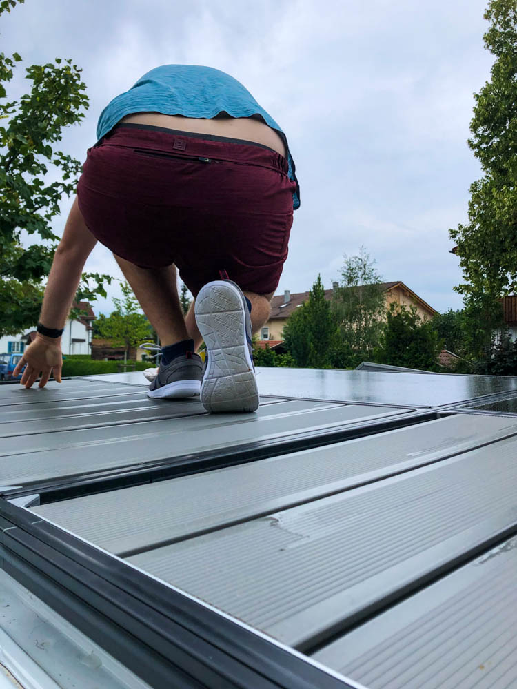 Julian sitzt auf dem Dach und reinigt die Solarpanels. Putzen und in Stand halten gehört zum Vanlife Alltag.
