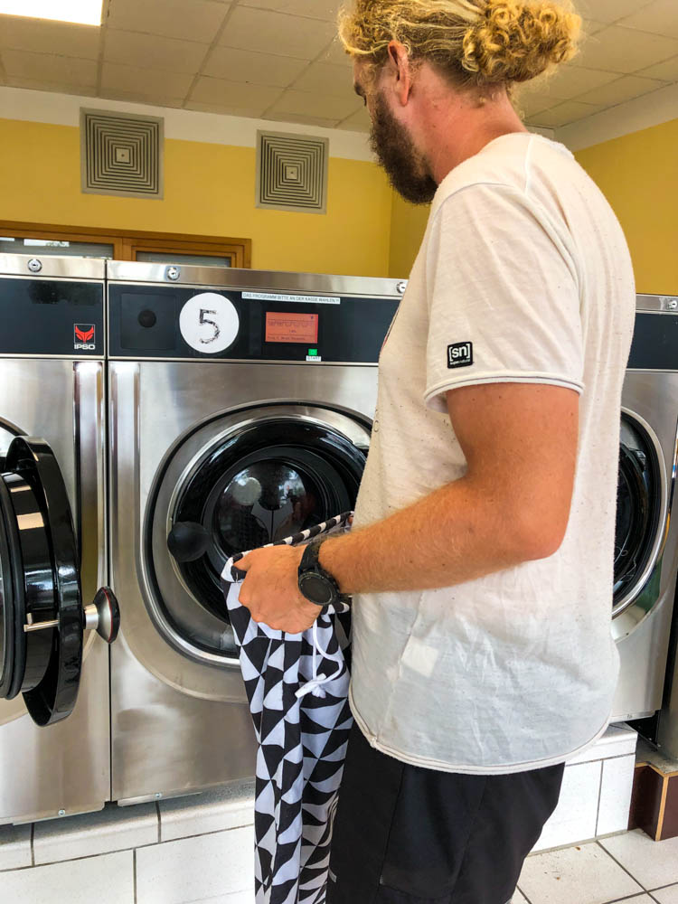 Julian steht vor einer Waschmaschine und sucht das richtige Programm. Im Vanlife Alltag ist das Thema Wäschewaschen auf dem Programm.
