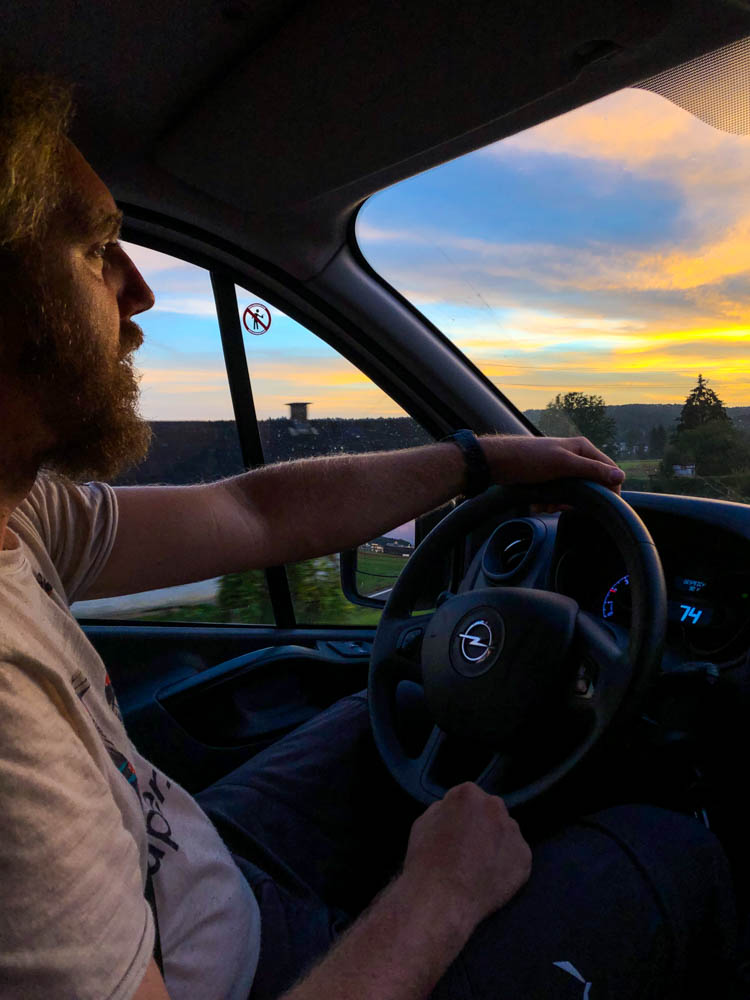 Julian sitzt am Steuer und fährt in den Sonnuntergang. Fahren gehört zum Vanlife Alltag dazu, da man immer in Bewegung ist.