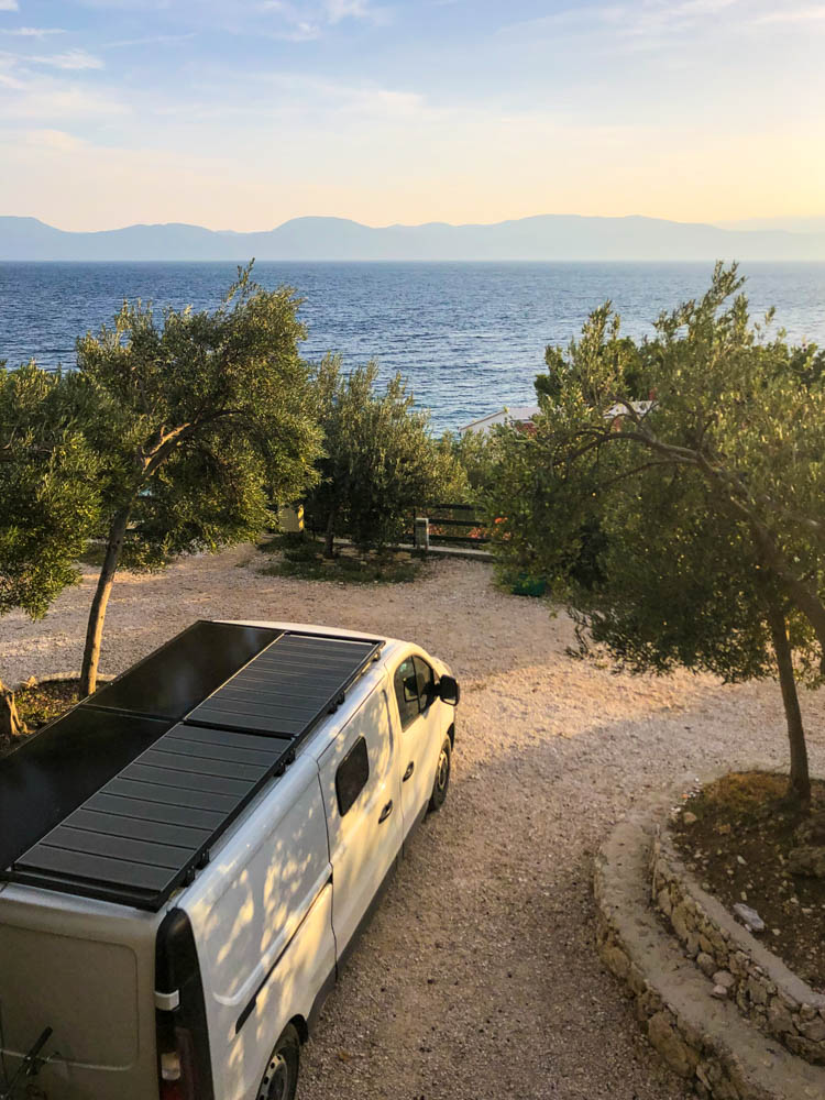 Van Vivaldi steht auf einem Campingplatz in Kroatien. Aufnahme von einer Ebene höher auf den Van und das Meer in der Abendsonne