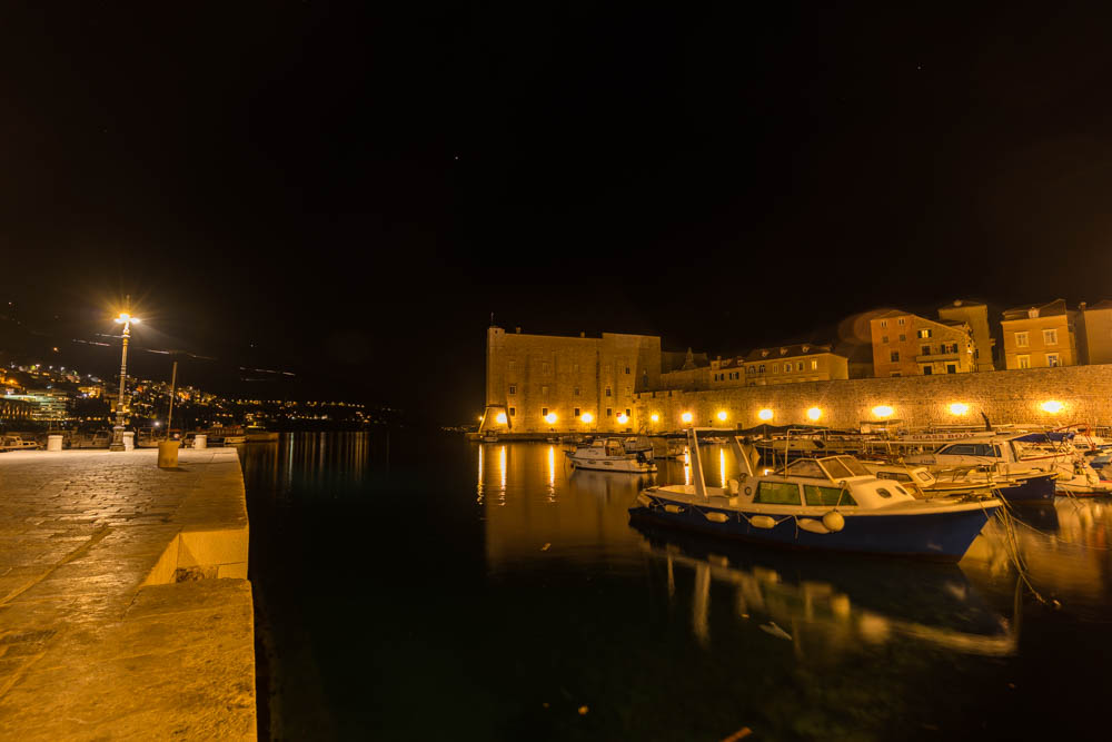 Nachtaufnahme in Dubrovnik mit Stadtmauer und ein paar Booten im Wasser. Städtetrips in Kroatien