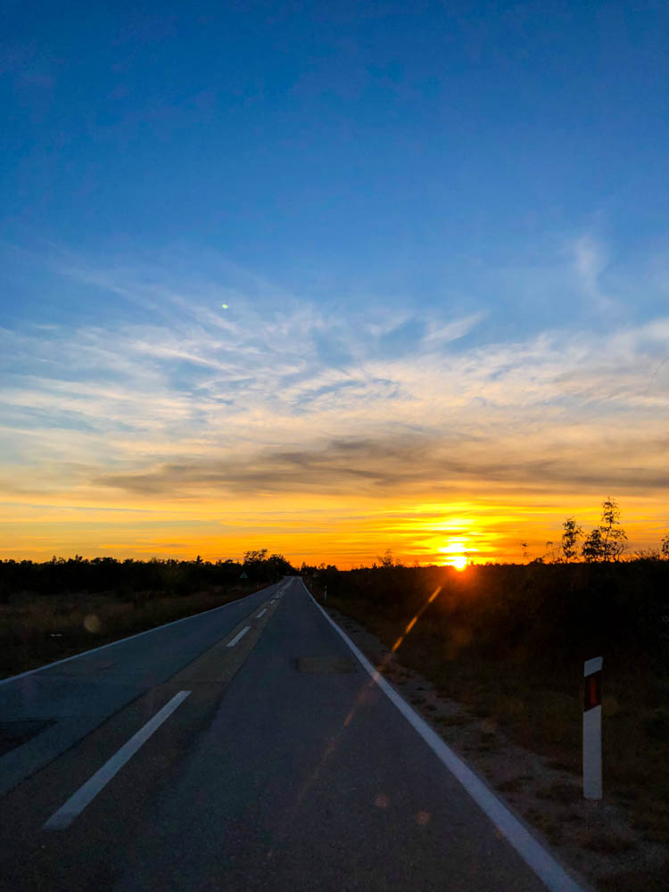 Sonnenuntergang im Krka Nationalpark, als wir mit dem Auto zum Schlafplatz gefahren sind. Vor uns liegt die Straße und wir fahren direkt in den Sonnenuntergang.