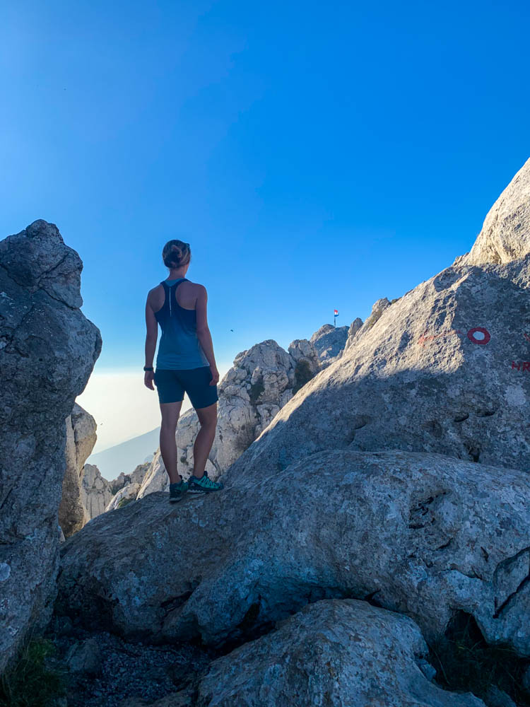 Melanie steht auf einem Felsvorsprung am Tulove Grede und Blickt auf den vor ihr liegenden Gipfel. Der Himmel ist strahlend blau.