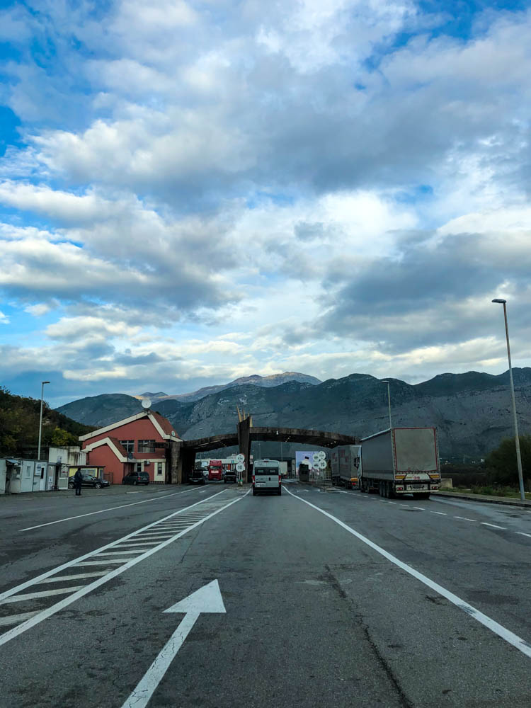 Grenze von Montenegro nach Albanien. Es sind ein paar wenige LKWs sowie Autos zu sehen sowie die Berge am Horizont.