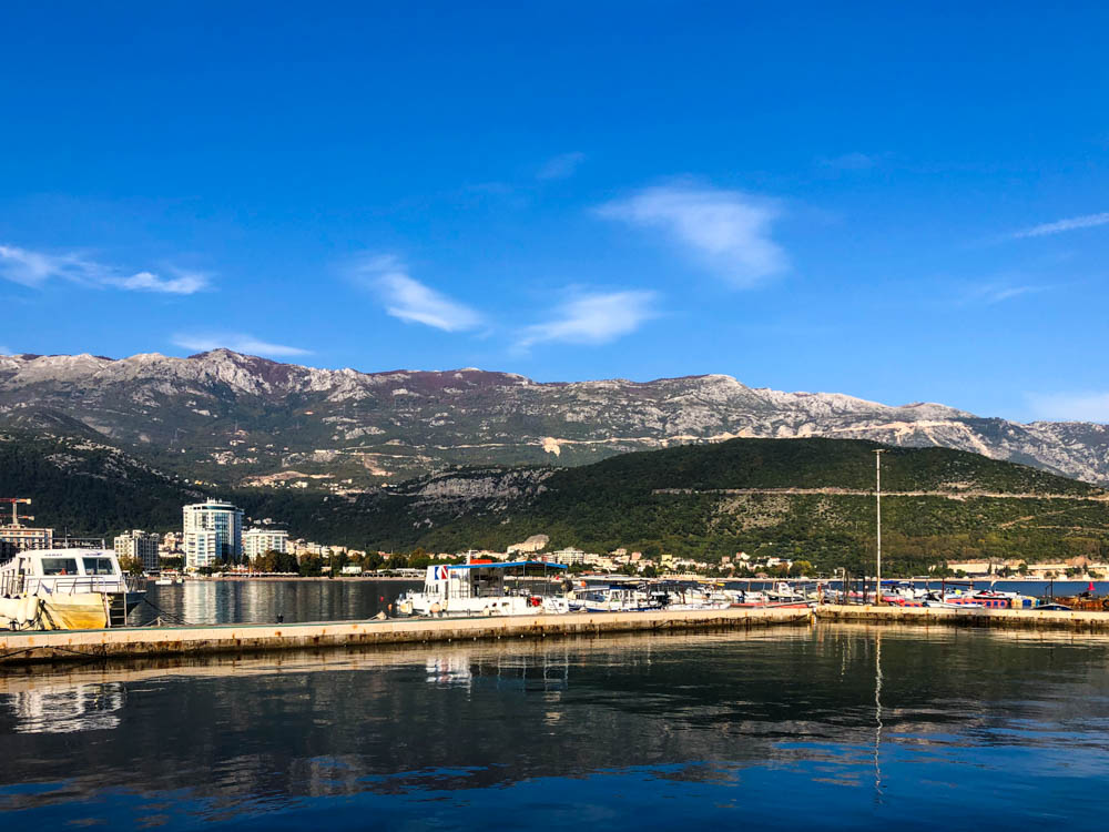 Budva Hafen Montenegro. Die Berge türmen sich direkt hinter der Stadt auf. Der Himmel ist kräftig blau.