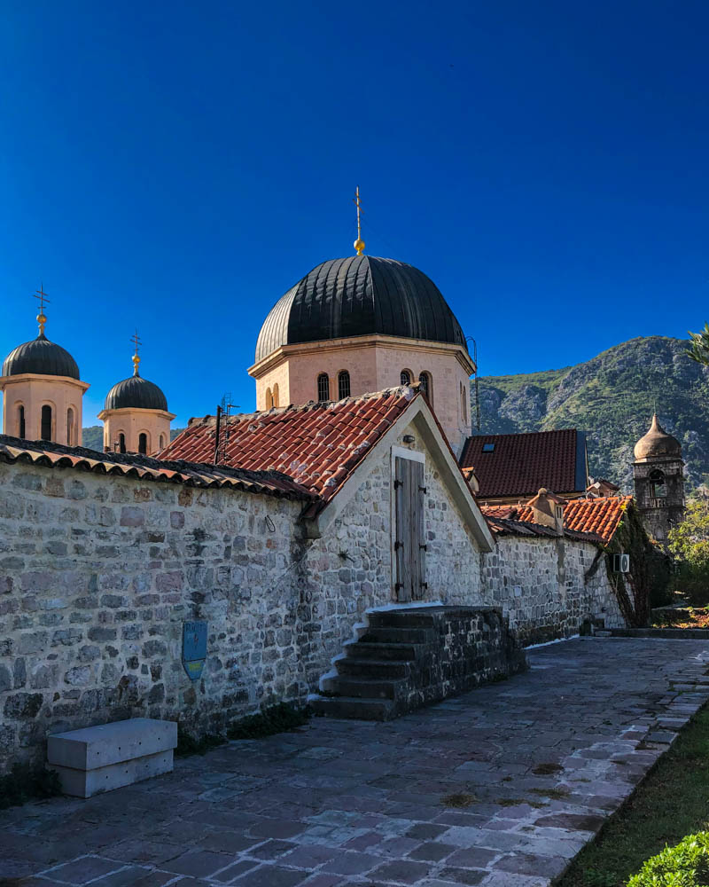 Kloster in Kotor mit mehreren Rundtürmen, welches von einer Steinmauer umgeben ist. Der Himmel ist kräftig blau. Roadtrip Montenegro