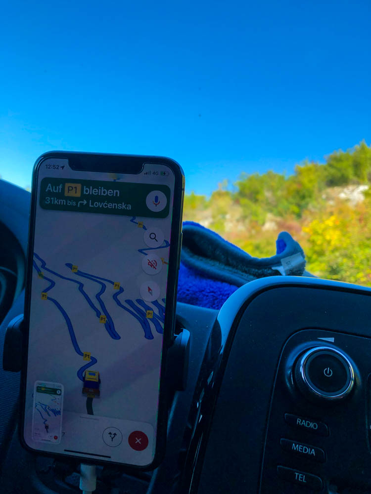 Kotor Pass - Es ist ein Handy mit einer Navigation zu sehen, welche die Serpentinen des Passes zeigt. Der Himmel ist kräftig blau