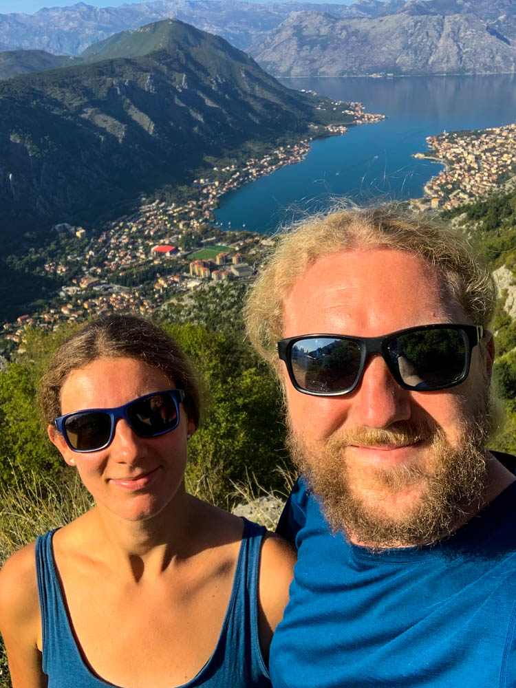 Selfie von Melanie und Julian am Kotor Pass. Hinter ihnen ist Kotor bzw. die Kotor Bucht zu sehen sowie die Hügelketten, welche den "Fjord" umgeben. Roadtrip Montenegro