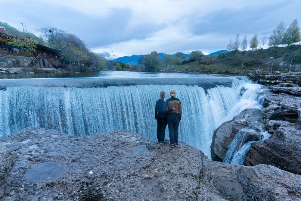 Melanie und Julian stehen vor den Niagara Fällen Montenegros. Ein breiter Wasserfall ist vor ihnen zu sehen. Roadtrip Montenegro