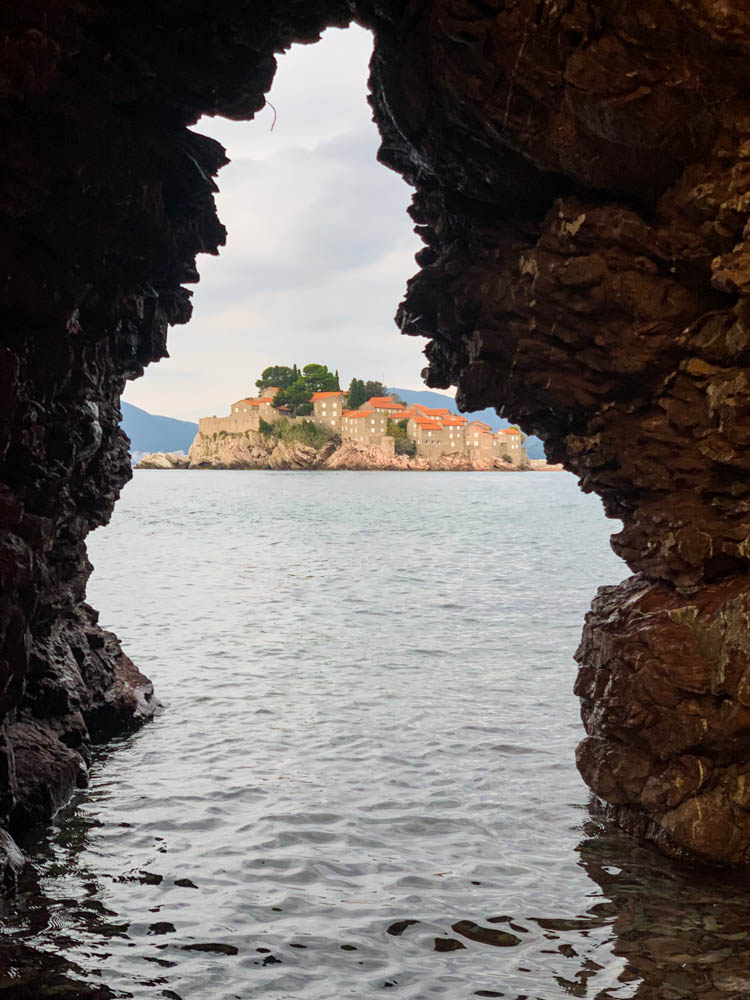 Durch eine Felsformation ist die Stadt Sveti Stefan zu sehen, welche eine Insel im Mittelmeer ist. Roadtrip Montenegro