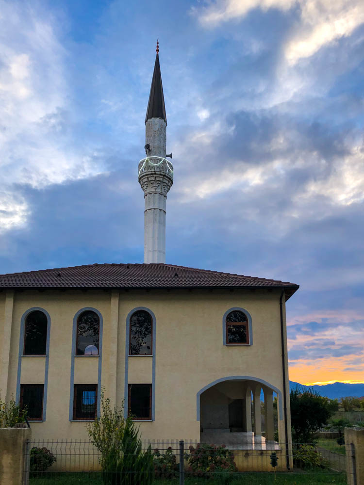Moschee in Albanien, dahinter geht die Sonne unter und der Himmel ist orange verfärbt.
