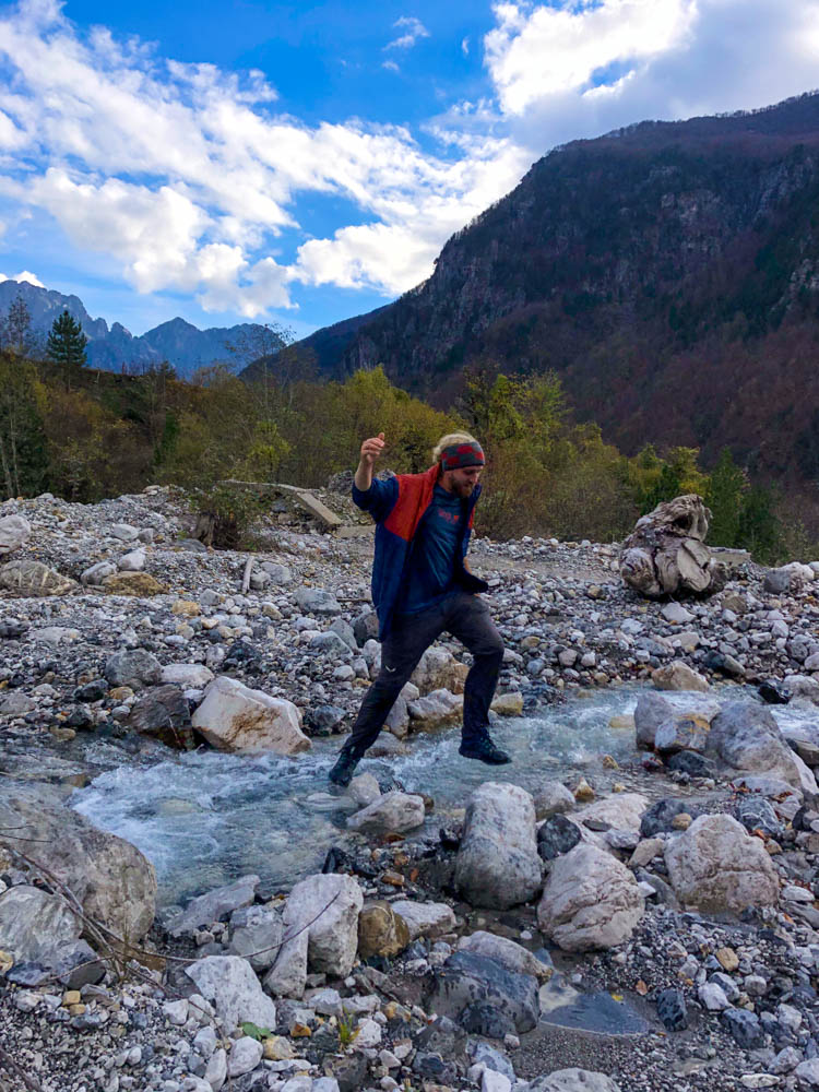 Julian springt über einen Bach in Theth, beim erkunden der Umgebung. Albanien Gebirge