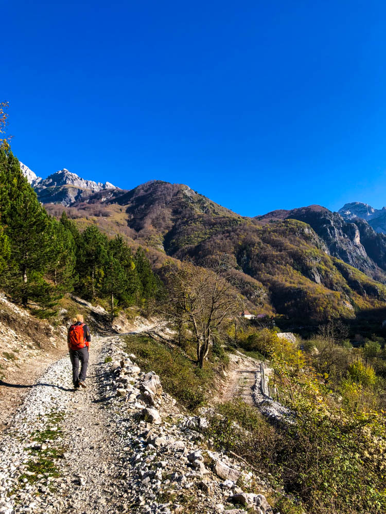 Julian beim Wandern in Albanien bei Theth. Es sind einige Berge und Hügel vor ihm zu sehen. Der Himmel ist kräftig blau.