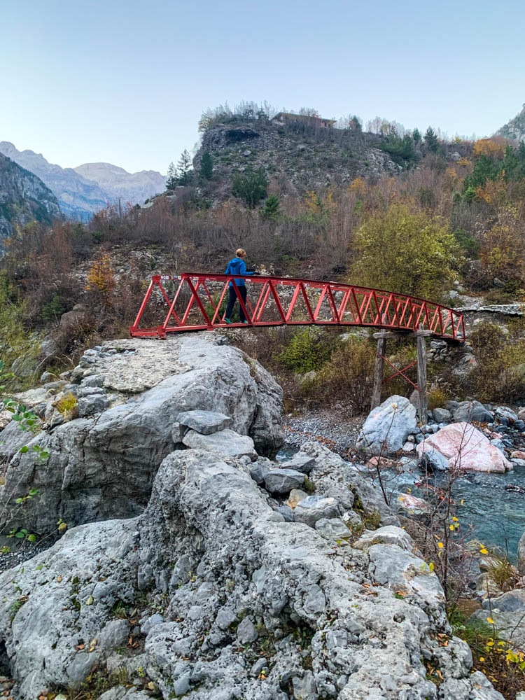 Rote Brücke über eine Schlucht. Melanie läuft über diese Brücke. Albanische Gebirgslandschaft.